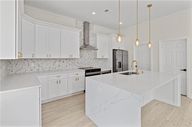 kitchen with stainless steel appliances, sink, white cabinets, wall chimney exhaust hood, and a kitchen island with sink