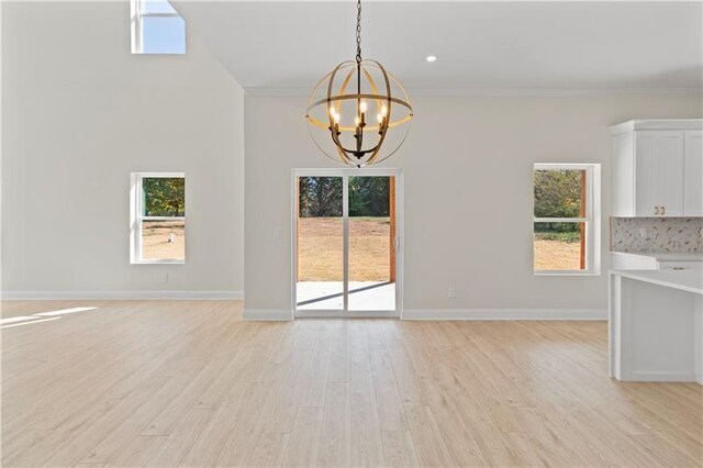 unfurnished dining area featuring a notable chandelier, light wood-type flooring, and crown molding