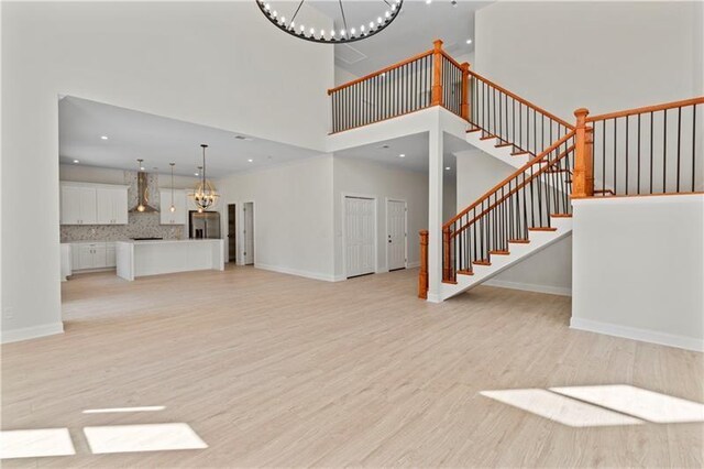 unfurnished living room with a high ceiling, light hardwood / wood-style floors, and a notable chandelier