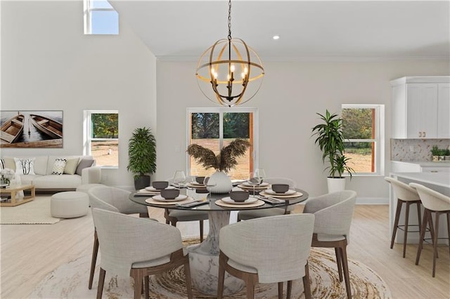 dining space with light wood-type flooring, an inviting chandelier, ornamental molding, and a wealth of natural light