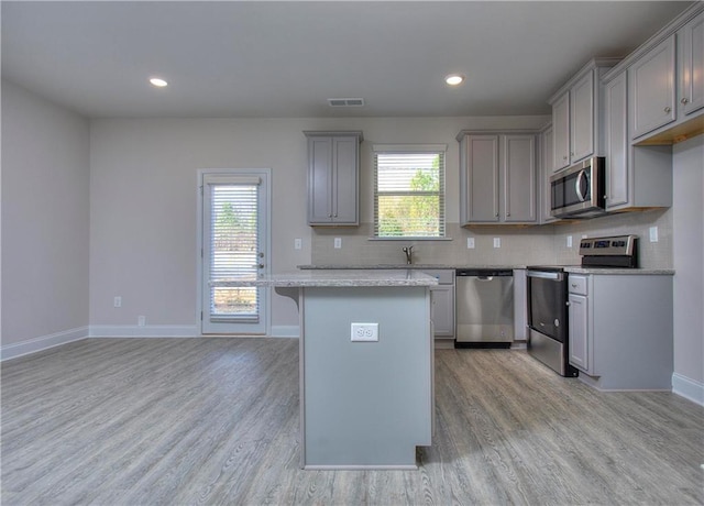 kitchen with light wood-type flooring, appliances with stainless steel finishes, gray cabinets, a kitchen island, and decorative backsplash