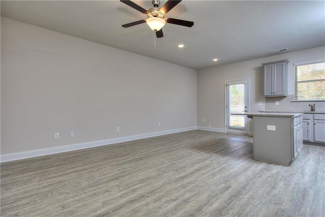 kitchen with sink, gray cabinetry, light stone counters, a kitchen island, and light hardwood / wood-style floors