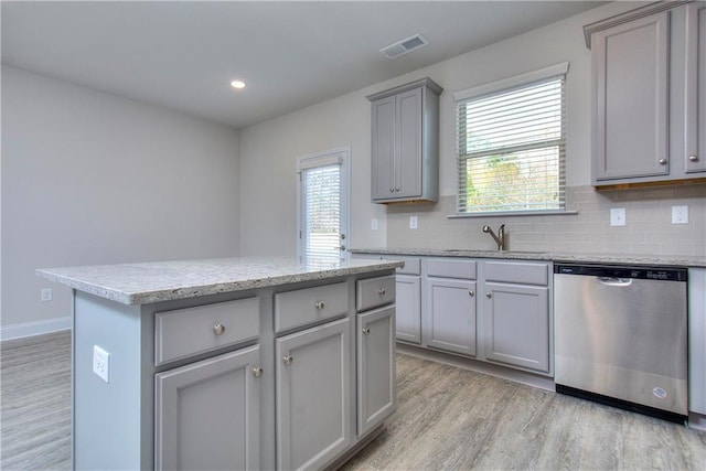 kitchen with sink, light hardwood / wood-style flooring, dishwasher, a kitchen island, and backsplash