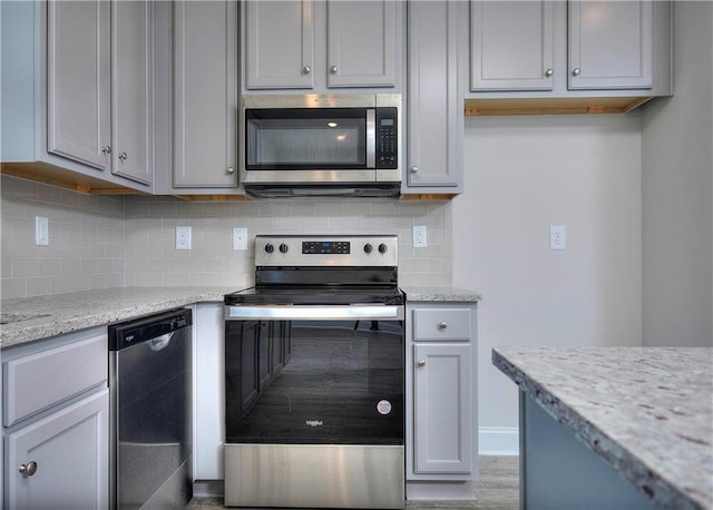 kitchen featuring tasteful backsplash, stainless steel appliances, light stone countertops, and gray cabinetry