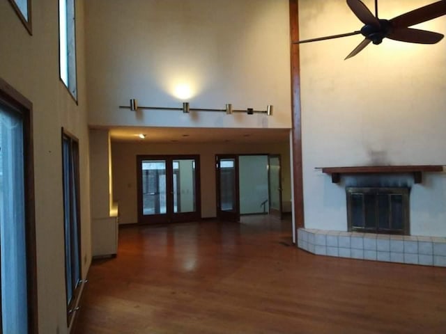 unfurnished living room featuring ceiling fan, a tile fireplace, dark wood-type flooring, and a towering ceiling