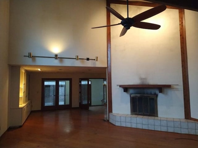 unfurnished living room featuring ceiling fan, dark wood-type flooring, a tiled fireplace, and a high ceiling