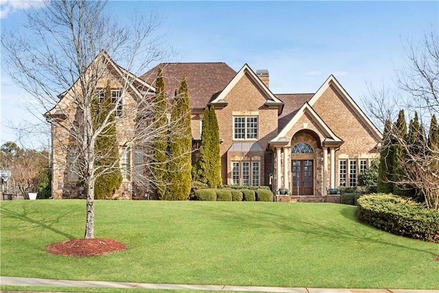 view of front of home with a front yard, brick siding, a chimney, and french doors