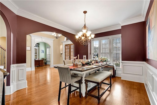 dining area with arched walkways, wainscoting, a notable chandelier, and wood finished floors