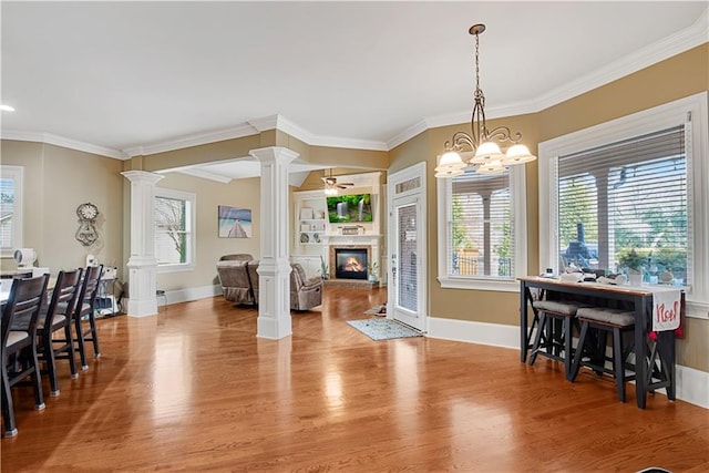 dining area featuring crown molding, a glass covered fireplace, decorative columns, and wood finished floors