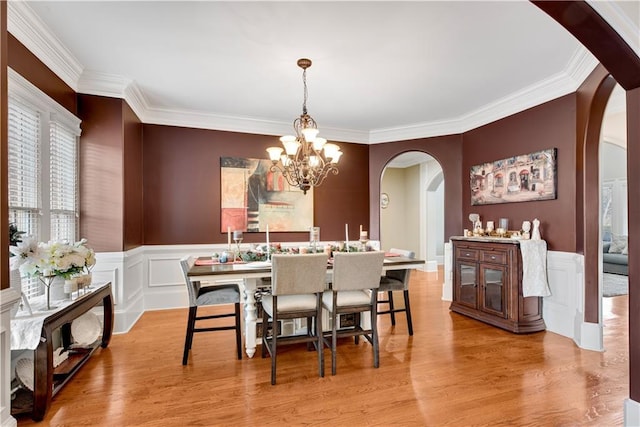 dining area featuring a chandelier, arched walkways, ornamental molding, and wood finished floors