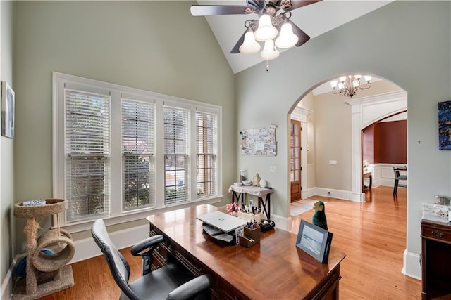 office area featuring light wood-style floors, arched walkways, vaulted ceiling, and ceiling fan with notable chandelier