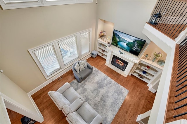 living room featuring wood finished floors, a glass covered fireplace, and a towering ceiling