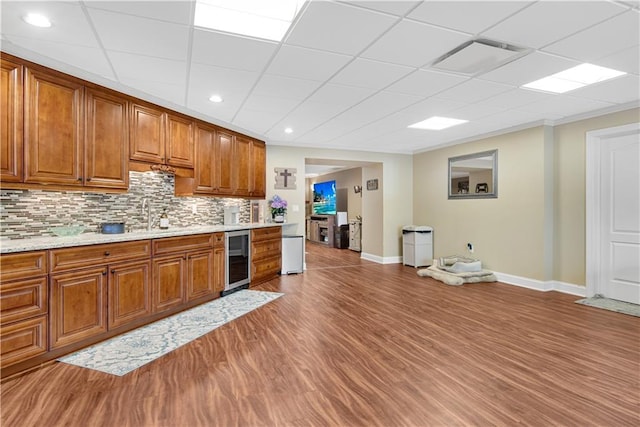 kitchen with beverage cooler, baseboards, light wood-style floors, tasteful backsplash, and brown cabinetry