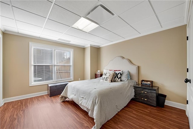 bedroom with a paneled ceiling, baseboards, and wood finished floors