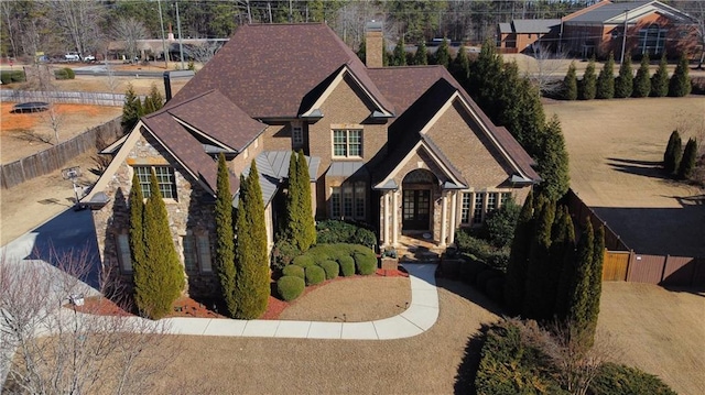 view of front of home featuring a shingled roof, stone siding, fence, and a chimney