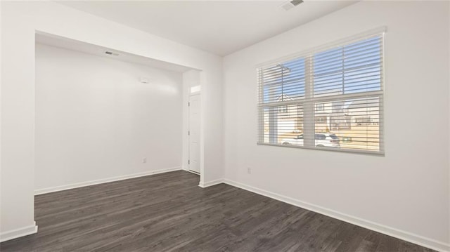 empty room featuring baseboards, dark wood-style floors, and visible vents