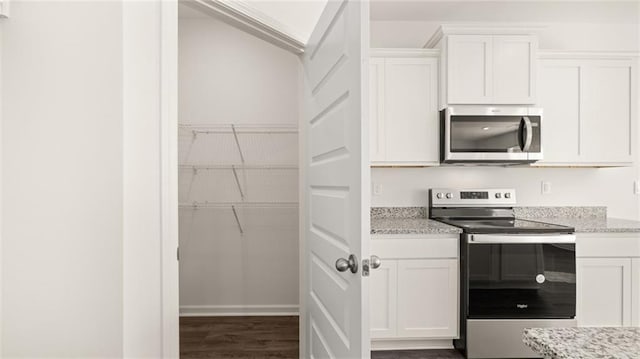 kitchen with dark wood finished floors, white cabinets, light stone countertops, and appliances with stainless steel finishes
