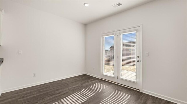 unfurnished room with baseboards, dark wood-style flooring, and visible vents