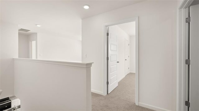 hallway featuring baseboards, visible vents, recessed lighting, and light colored carpet