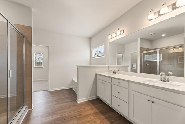 bathroom featuring a stall shower, double vanity, a sink, and wood finished floors