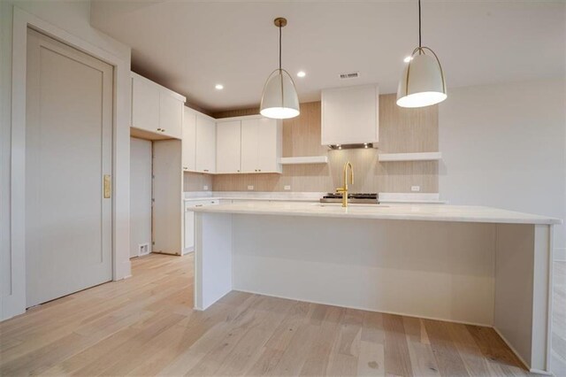 kitchen featuring visible vents, light countertops, light wood-type flooring, a large island with sink, and backsplash