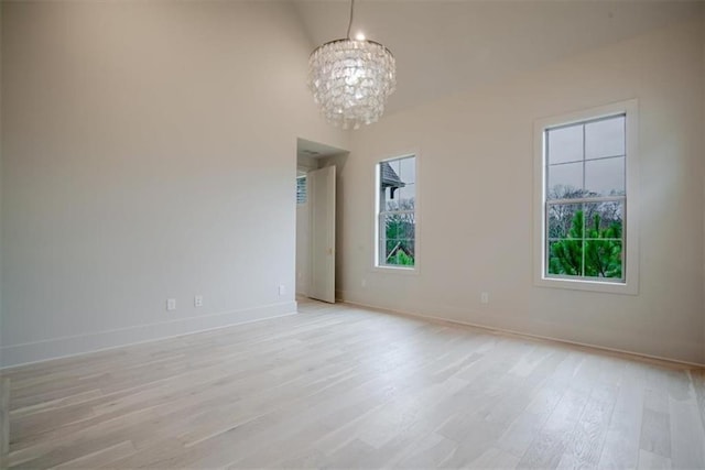 spare room featuring a chandelier, a wealth of natural light, light wood-style floors, and baseboards