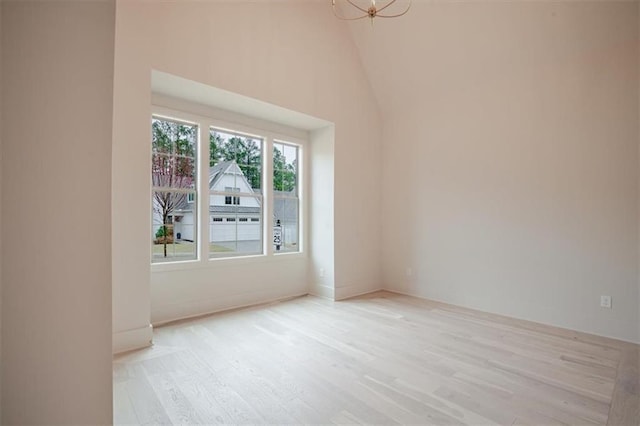unfurnished room with high vaulted ceiling, light wood-style flooring, and an inviting chandelier