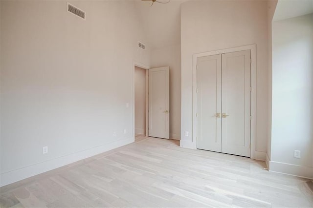 unfurnished bedroom with visible vents, baseboards, a high ceiling, and light wood-style flooring
