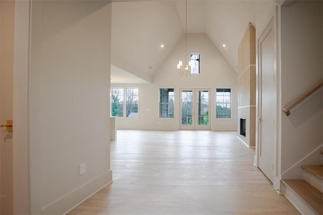 unfurnished living room with a chandelier, a fireplace, stairway, light wood-style flooring, and high vaulted ceiling