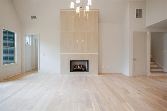 unfurnished living room with stairway, light wood finished floors, visible vents, and an inviting chandelier