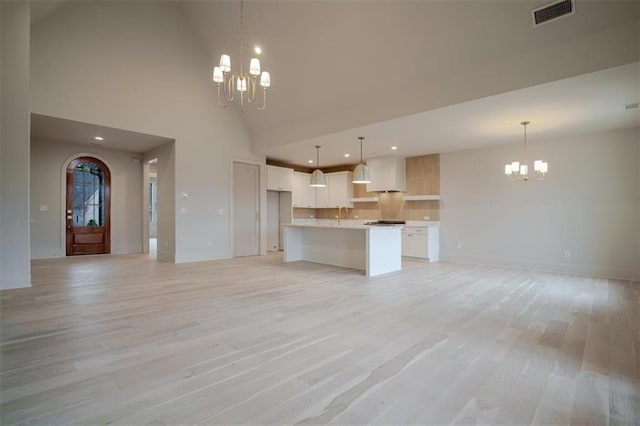 unfurnished living room with visible vents, baseboards, light wood-type flooring, a chandelier, and a towering ceiling