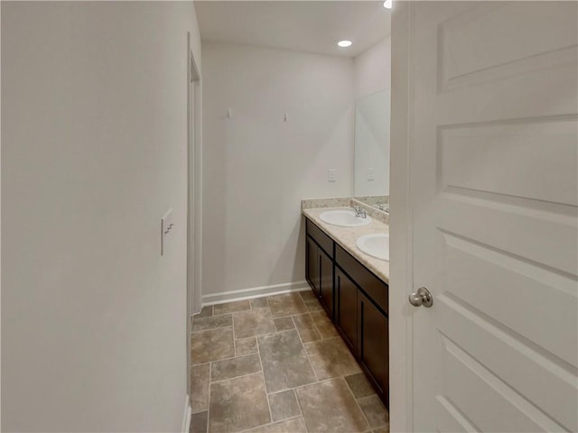 bathroom featuring double vanity, stone finish floor, a sink, and baseboards