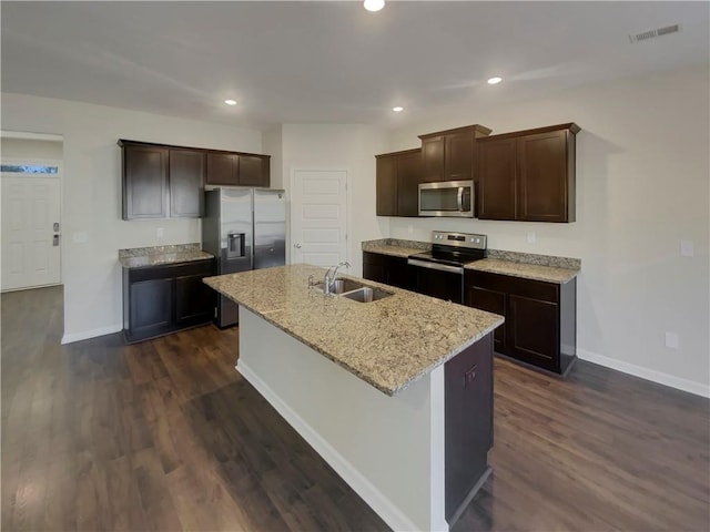 kitchen with dark wood-type flooring, a sink, baseboards, appliances with stainless steel finishes, and an island with sink