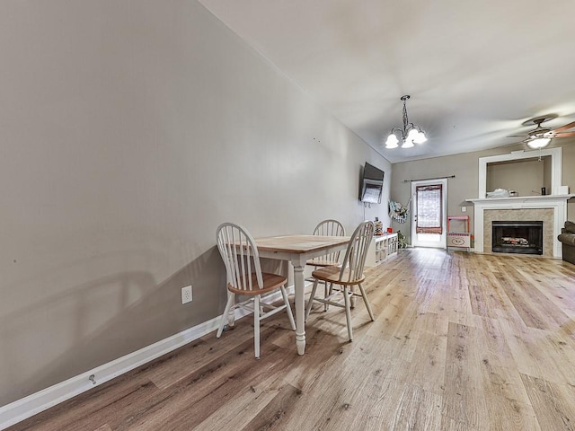 dining room featuring ceiling fan with notable chandelier, a tiled fireplace, and light hardwood / wood-style floors