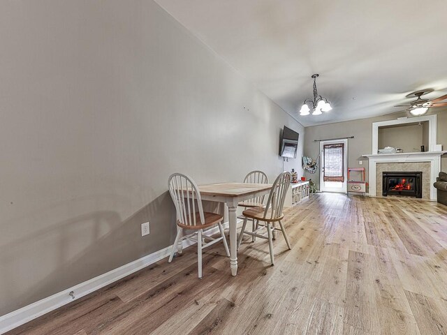 dining area with light hardwood / wood-style floors, ceiling fan with notable chandelier, and a fireplace