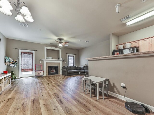 living room with ceiling fan with notable chandelier, a tiled fireplace, and light hardwood / wood-style floors