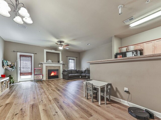 interior space featuring a tile fireplace, ceiling fan with notable chandelier, and light hardwood / wood-style floors