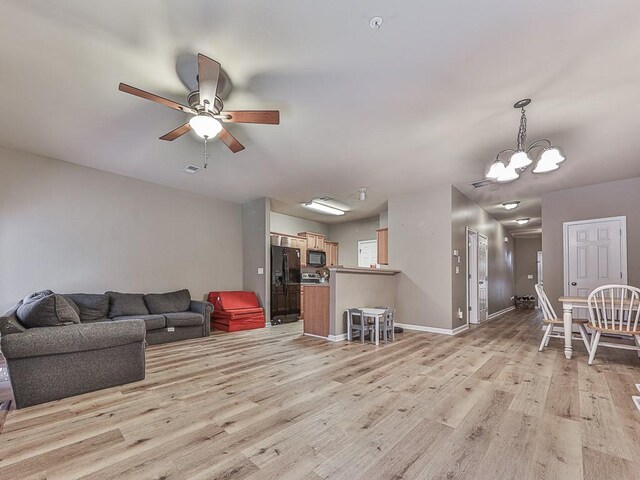 living room featuring ceiling fan with notable chandelier and light hardwood / wood-style floors