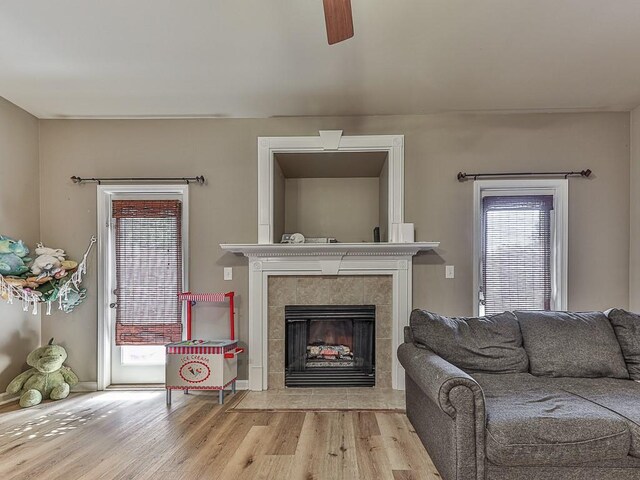 living room featuring a tile fireplace, light hardwood / wood-style floors, and ceiling fan