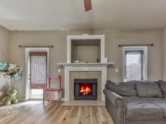 living room with light hardwood / wood-style flooring, ceiling fan, and a tile fireplace