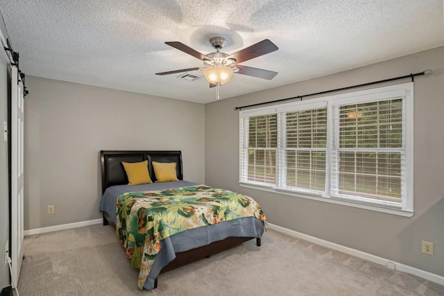 bedroom with ceiling fan, a barn door, light colored carpet, and a textured ceiling