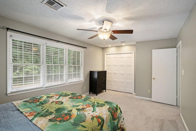 bedroom featuring ceiling fan, a closet, light carpet, and a textured ceiling