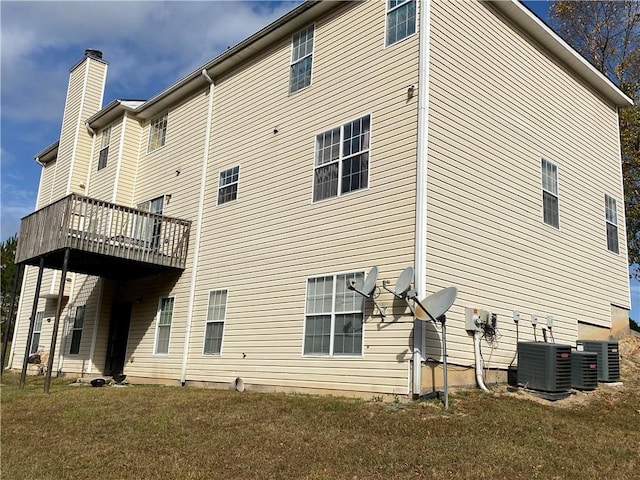 rear view of property with central AC unit and a lawn