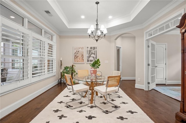 dining room featuring a raised ceiling, dark hardwood / wood-style floors, an inviting chandelier, and ornamental molding