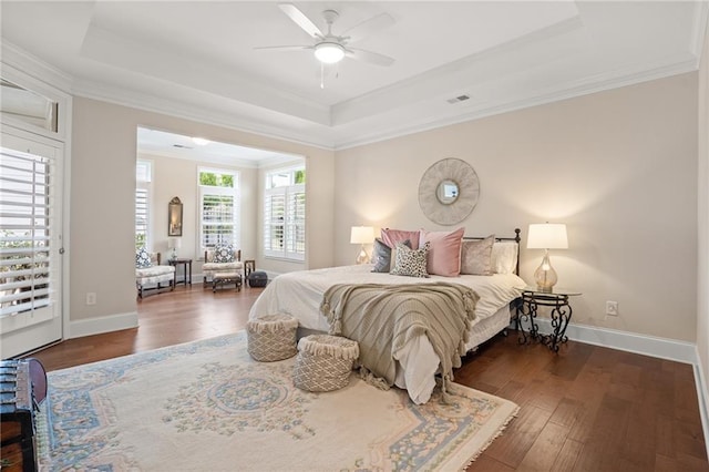 bedroom with ceiling fan, ornamental molding, dark wood-type flooring, and a tray ceiling