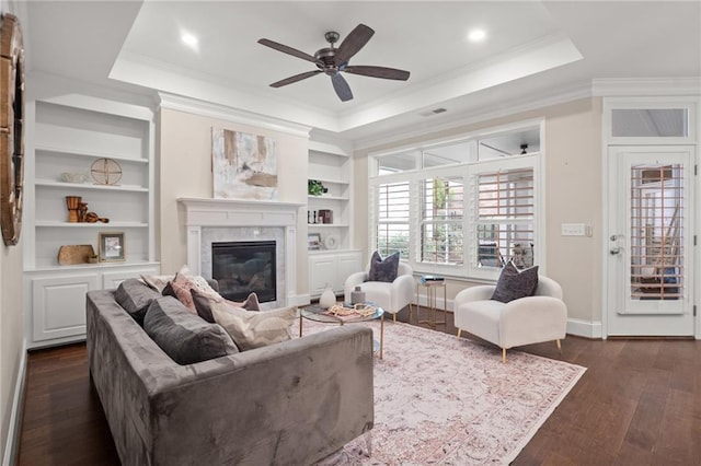 living room with a high end fireplace, ceiling fan, ornamental molding, a tray ceiling, and dark hardwood / wood-style flooring