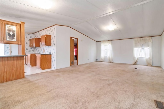 unfurnished living room featuring visible vents, ornamental molding, light carpet, vaulted ceiling, and wallpapered walls