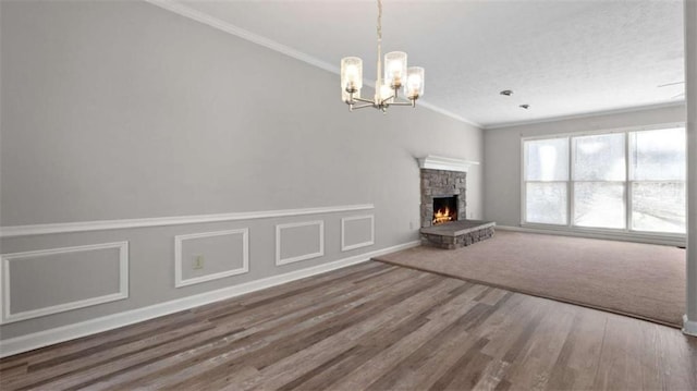 unfurnished living room with ornamental molding, wood finished floors, an inviting chandelier, a stone fireplace, and a decorative wall