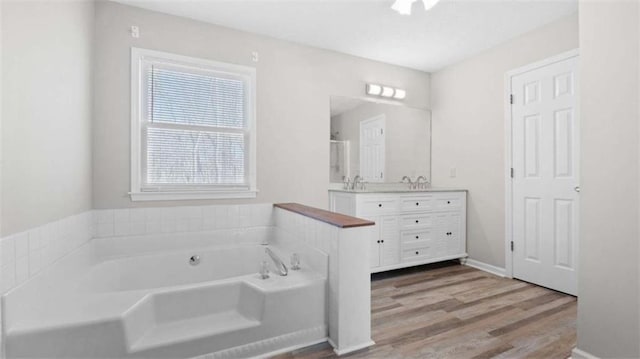 bathroom featuring a garden tub, baseboards, wood finished floors, and vanity