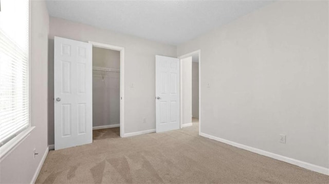 unfurnished bedroom with a spacious closet, a closet, baseboards, and carpet flooring